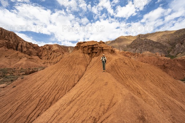 Mountaineer on a mountain ridge, eroded mountain landscape with sandstone rocks, canyon with red