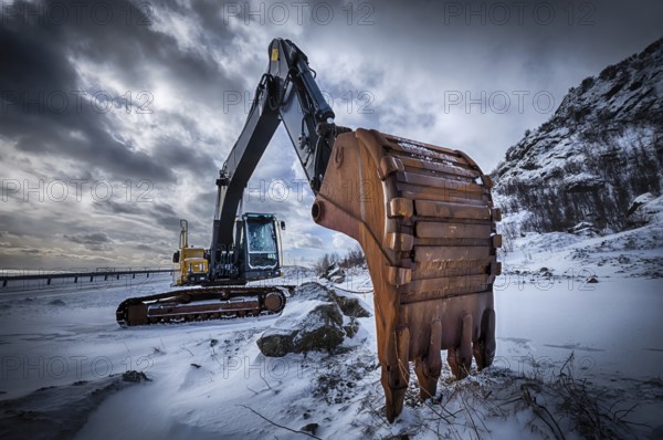Old excavator with excavator bucket in winter. Road construction in snow. Lofoten islands, Norway.