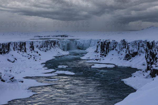 Selfoss waterfall with the river Jökullsa a Fjöllum, icy and snow-covered cliffs and shoreline,