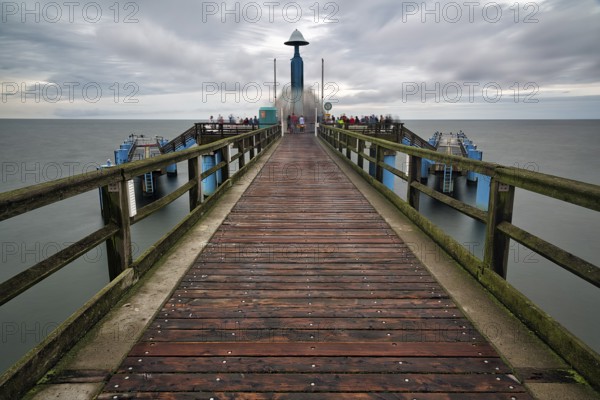 Sellin pier with tourists in front of diving gondola, rainy weather on the Baltic Sea, long