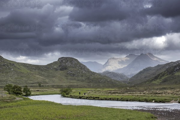 Two walkers walking on path along river and rain clouds forming in Wester Ross, Scottish Highlands,