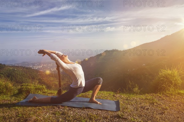 Yoga outdoors, sporty fit woman practices yoga Anjaneyasana, low crescent lunge pose outdoors in