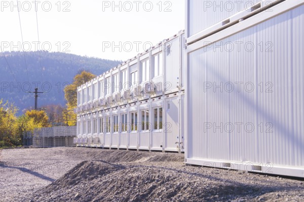 Row of white containers along a gravel path, illuminated by sunlight, refugee accommodation