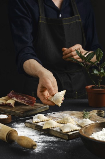 A person in an apron carefully shapes filled pasta in a warmly lit kitchen. Flour dust covers the
