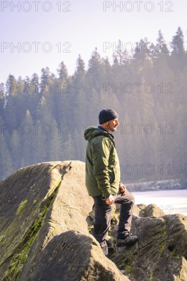 Man with outdoor clothes standing on a rock, surrounded by forest and sunlight, Glaswaldsee, Bad