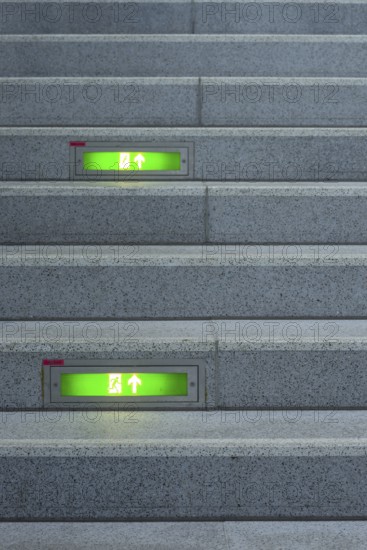 Public staircase with green illuminated emergency exit signs, Germany, Europe