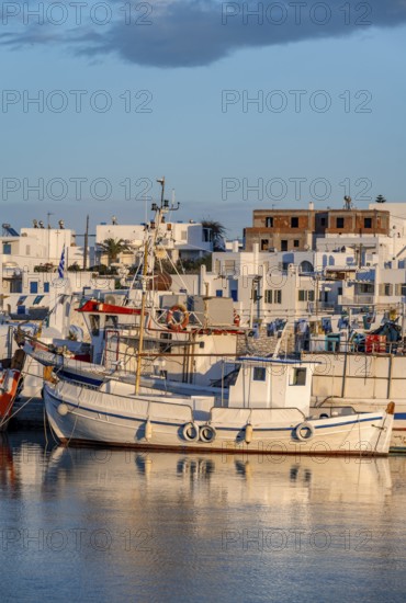 Fishing boats in the harbour at sunset, reflected in the sea, White Cycladic houses, Naoussa,