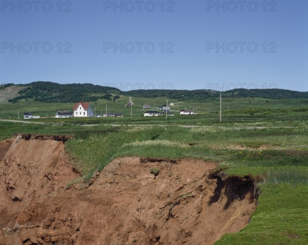 Cliff with eroded soil and houses in the distance in summer, Havre-Aubert, Magdalen Islands,