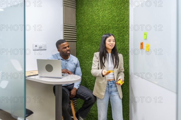 Two managers are discussing a project using sticky notes on a whiteboard in a modern coworking