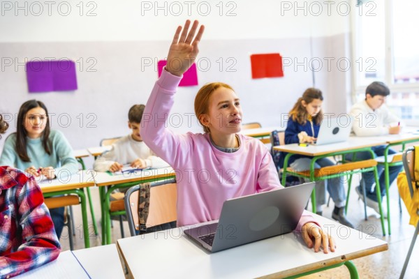Smart student raising hand to answer teacher's question in modern classroom with laptops and