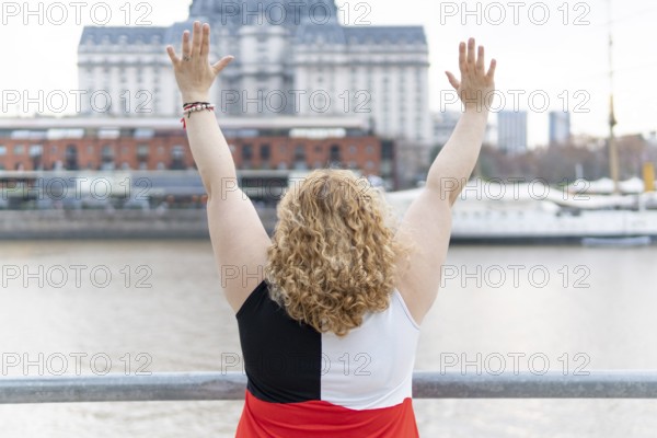 Plus size blonde woman on her back standing on the waterfront with her arms outstretched