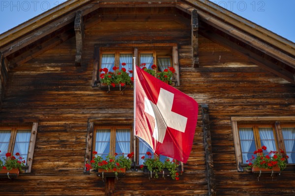 Beautiful Old Town with a Wood House with Flower and Swiss Flag in a Sunny Summer Day in Andermatt,