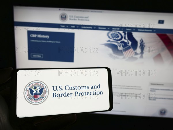Stuttgart, Germany, 10-29-2023: Person holding smartphone with seal of agency United States Customs