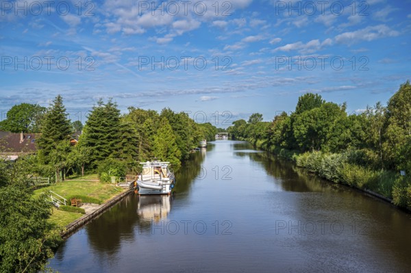 A canal surrounded by lush greenery under a slightly cloudy sky with a boat, Ems-Seitenkanal,