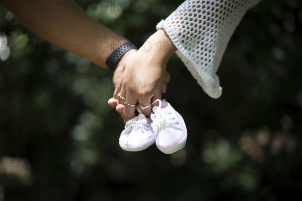 Detail of a couple's hands holding baby shoes