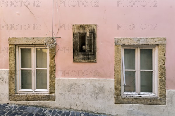 Facade of an old building with pastel pink walls and stone-framed windows with closed wooden