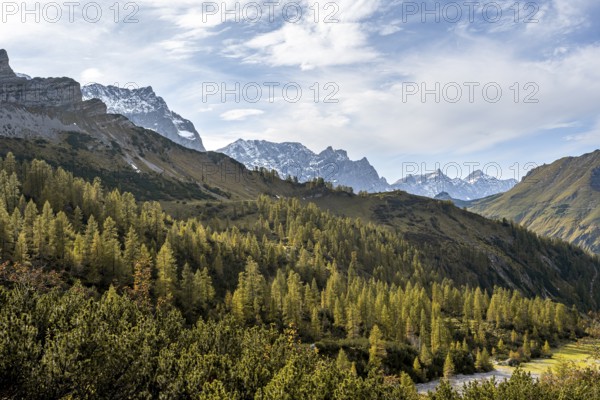 Mountain panorama with steep rocky peaks, yellow-coloured larches in autumn, hike to the summit of