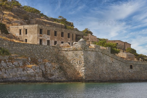 Dilapidated-looking old buildings on a rocky coastline surrounded by clear skies and calm seas,