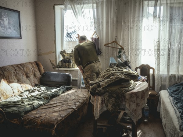 Gennady, 48 years old, stationed in Kupyansk, looking out of the window of the house where his unit