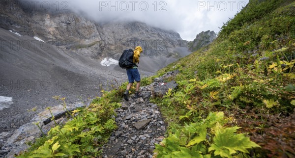 Mountaineer hiking in the mountains with yellow jacket, hiking trail to Valentintörl, cloudy