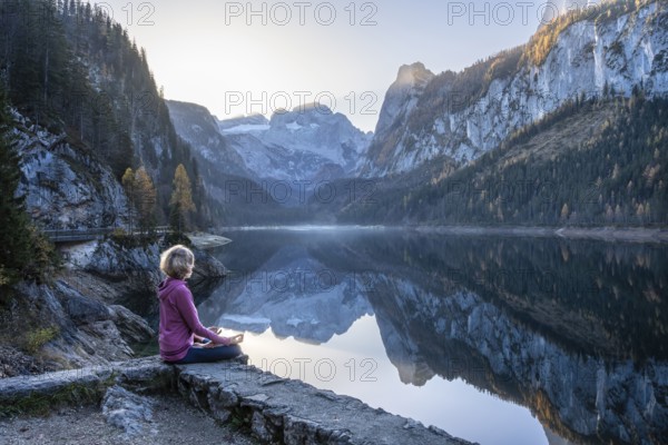 A woman doing yoga by the lake. Lotus position (Padmasana) . Vorderer Gosausee in autumn with a