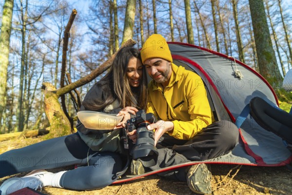 Couple of hikers reviewing photos on professional camera while having a meal in front of their tent