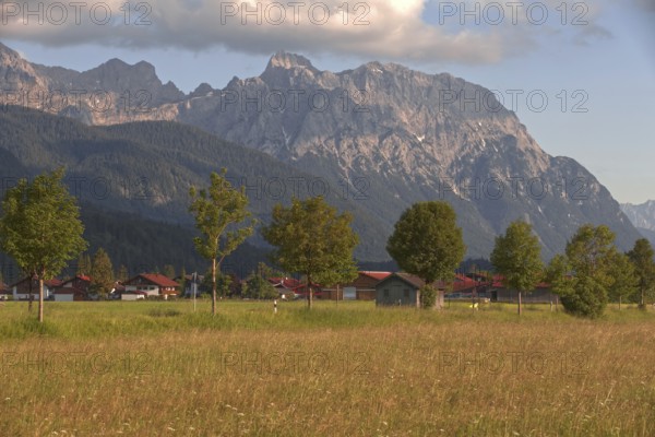 View of a village in front of majestic mountains, surrounded by green meadows and trees under a