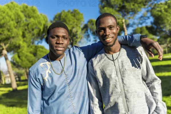 Two young senegalese men wearing traditional dashiki clothing embrace in a park, celebrating