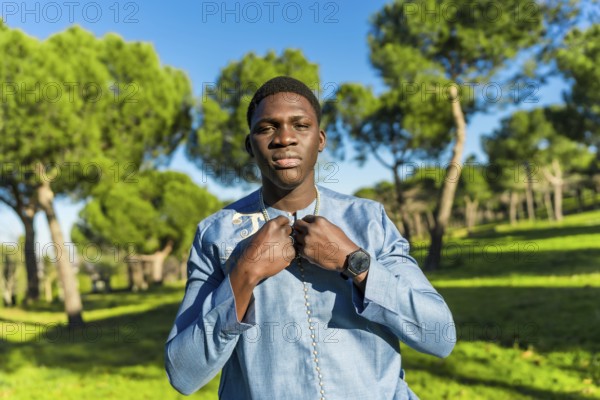 Young senegalese man wearing traditional dashiki attire, posing in a serene park setting,
