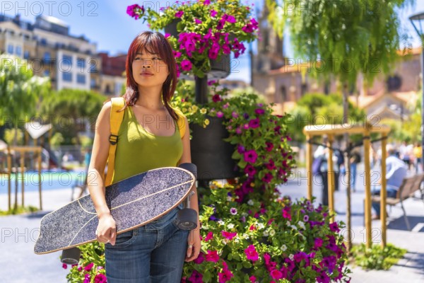 Portrait with copy space of a young chinese woman carrying skateboard on a city square full of