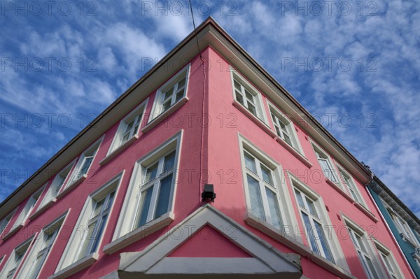 Historic building with pink facade and white window frames under a blue sky with light clouds,