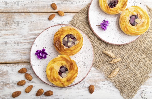 Small cheesecakes with jam and almonds with cup of coffee on a white wooden background and linen