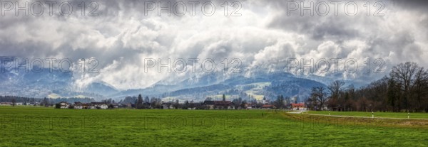 Green meadow and small village in the foreground, dramatic clouds, mountains in the background, Bad