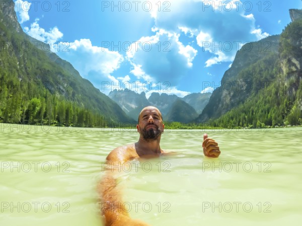 Tourist gesturing thumbs up while swimming in the turquoise water of lago di landro, surrounded by