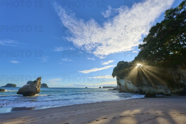 Landscape with sandy beach and bright sun behind rocks by the sea, Cathedral Cove, Coromandel,