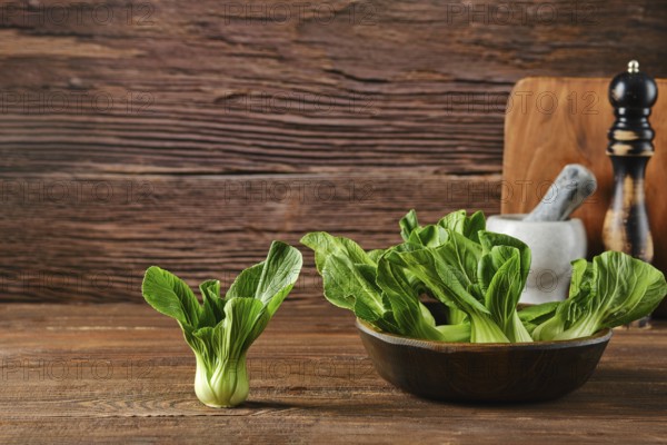 A bunch of vibrant bok choy sits in a bowl alongside a single piece on a wooden table, complemented