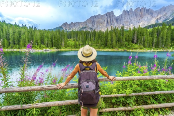 Female tourist with backpack admiring the stunning turquoise waters of lake carezza and the latemar