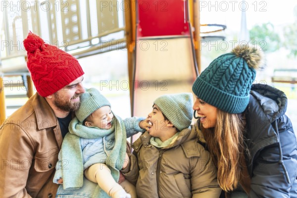 Happy family wearing winter clothes is having fun at the playground, enjoying precious moments