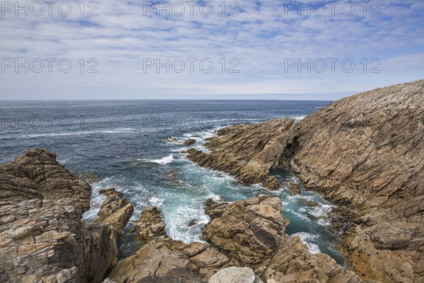 Rocky west coast of the Quiberon peninsula in Brittany, France, with a partly cloudy sky. Crashing