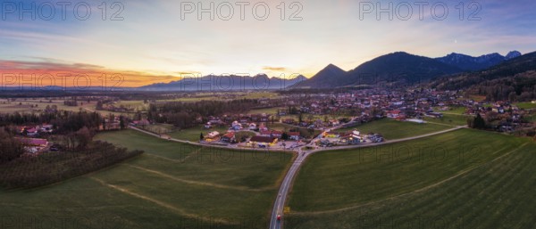 Panoramic view of a village in a wide green plain with mountains in the background at dusk, Bad