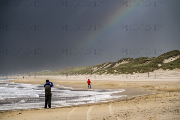 Walkers on the beach, dark storm clouds, choppy sea, autumn on the North Sea in North Holland,