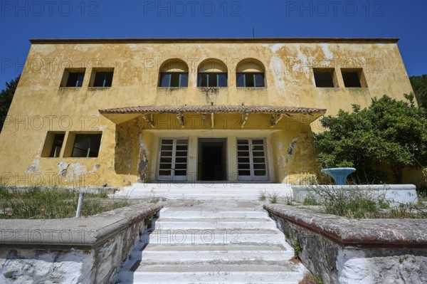 An abandoned building with a crumbling façade and an external staircase on a sunny day under a blue