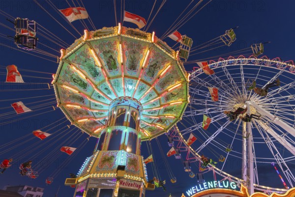 A funfair at dusk with illuminated chain carousel and Ferris wheel, Europa Rad, rides, wave flight,