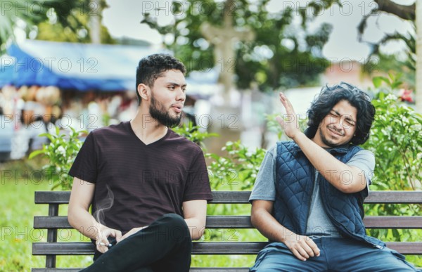 Man smoking and exhaling smoke to another person near him. Man smoking cigarette near people in