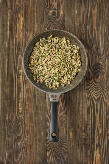 A skillet filled with sauteed diced mushrooms mixed with fresh herbs on a rustic wooden table. The