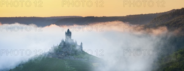 View of the Reichsburg Cochem with morning mist in the Moselle valley, Cochem,
