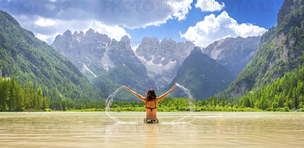 Young woman enjoying summer vacations, splashing water in the scenic lago di landro, surrounded by
