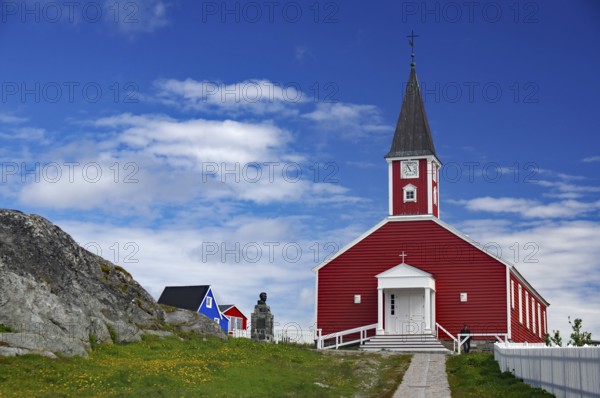 Red church with white entrance and tower, sculpture next door under a blue sky, Church of the