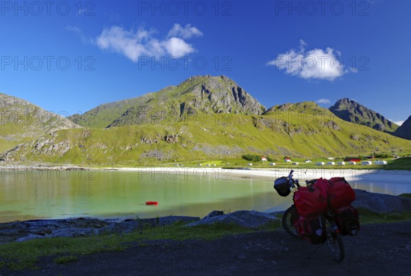 View of a bicycle with red bags on the shore of a bay, surrounded by green hills and mountains