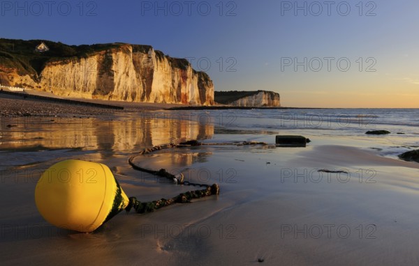 Chalk cliffs of the Alabaster Coast in the evening light, in front a yellow buoy on the beach at
